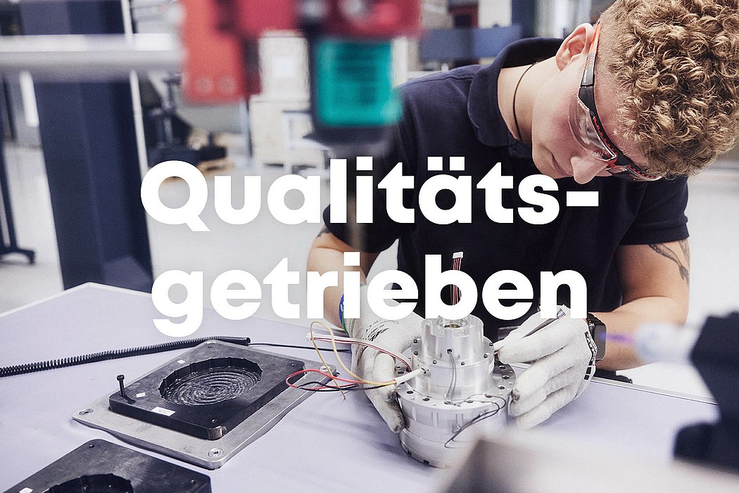 Ein Mitarbeiter von Agile Robots arbeitet mit Präzision an einem Bauteil und prüft die Qualität. Auf dem Bild steht „Qualitätsgetrieben“ geschrieben.