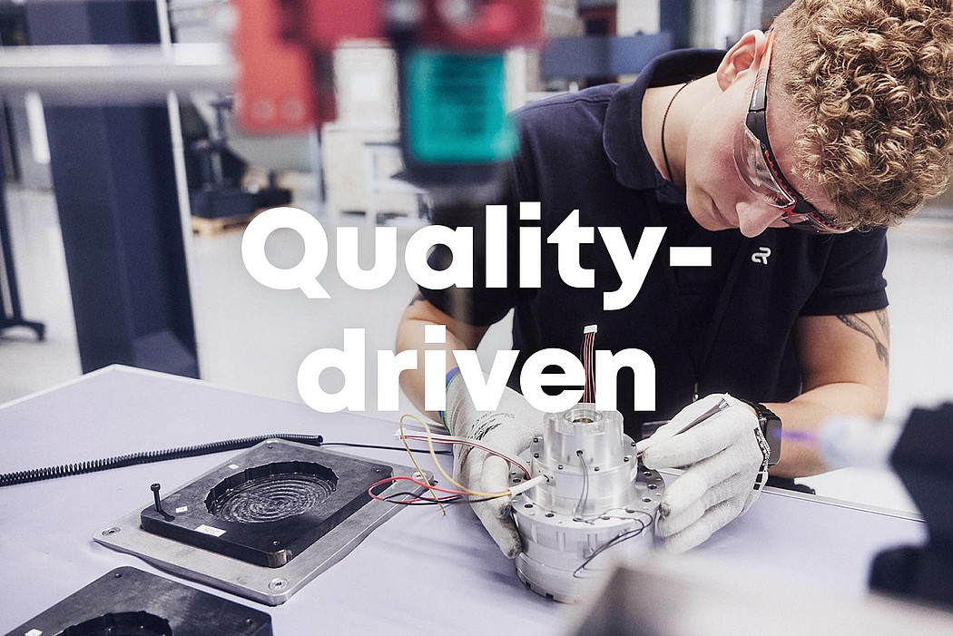 An Agile Robots employee working on a component with precision, inspecting for quality. The word “Quality driven” is written in the middle of the photo.